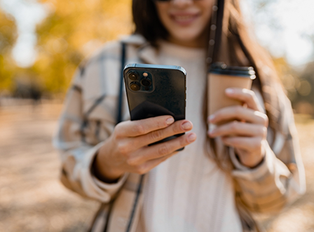 Woman looking at phone while carrying coffee