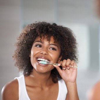 Woman smiling while brushing teeth in bathroom