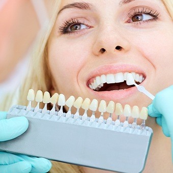 Cosmetic dentist holding a row of veneers up to a woman's smile