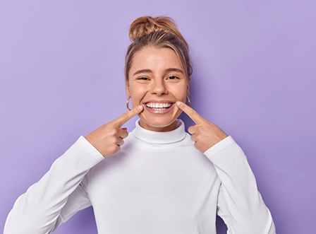 Woman in white sweater pointing to smile