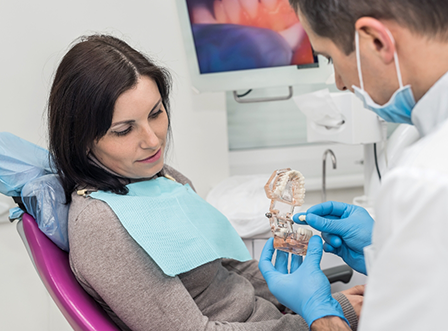 Dentist with mask showing dental crown to female patient