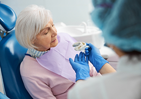 Senior woman in dental chair looking at model of dental implant restoration
