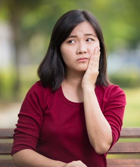 Woman holding her cheek in pain before visiting emergency dentist in Austin