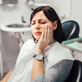 Woman in dental chair holding her cheek in pain