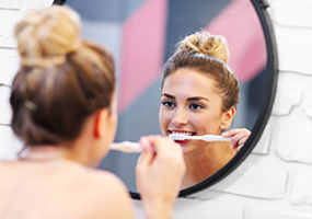 Woman brushing teeth in oval shaped mirror