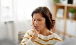 Woman in striped sweater rubbing jaw in pain