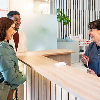 Dental receptionist smiling at couple in lobby