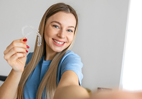 Woman holding Invisalign aligner and smiling