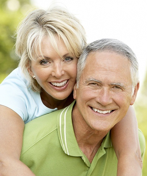 Smiling older man and woman outdoors after replacing missing teeth in Austin