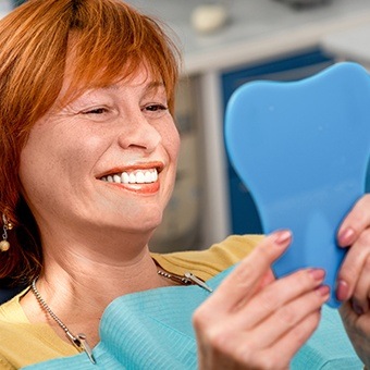 Older redheaded woman looking at her smile in mirror