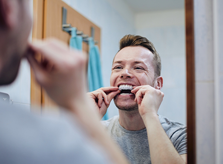 Man putting on nightguard in bathroom mirror