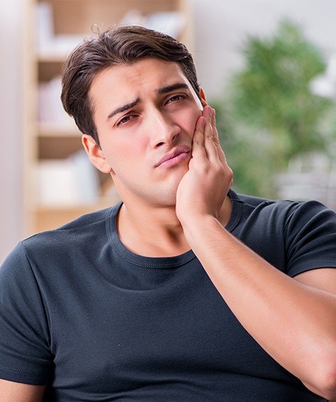 Man holding his cheek in pain before wisdom tooth extractions in Austin