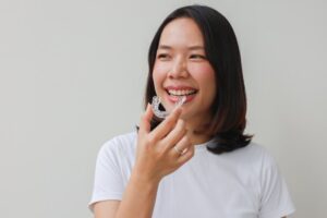 Woman smiling while putting in her Invisalign trays