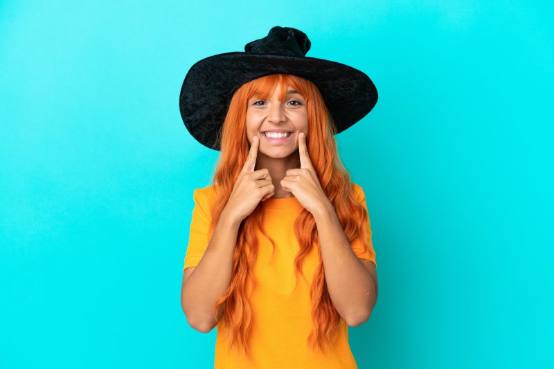 A young, smiling woman wearing a witch’s hat against a blue background