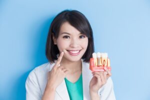 Dentist holding model of dental implant and pointing to her smile. 